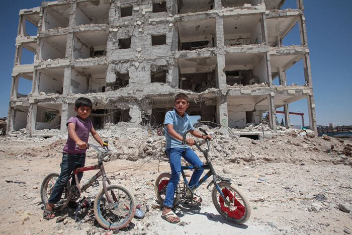 Дети позируют на своих велосипедах на фоне разрушенного здания в центре городе Кобан, Сирия. 20 июня 2015г.