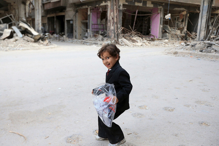 Мальчик несет сумку с новой одеждой перед праздником конца Рамадана. Окраины Дамаска, Сирия. 15 июля 2015г.