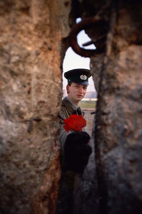 Охранник Берлинской стены,  в день, когда она была снесена, передаёт цветок через расщелину. (1989).