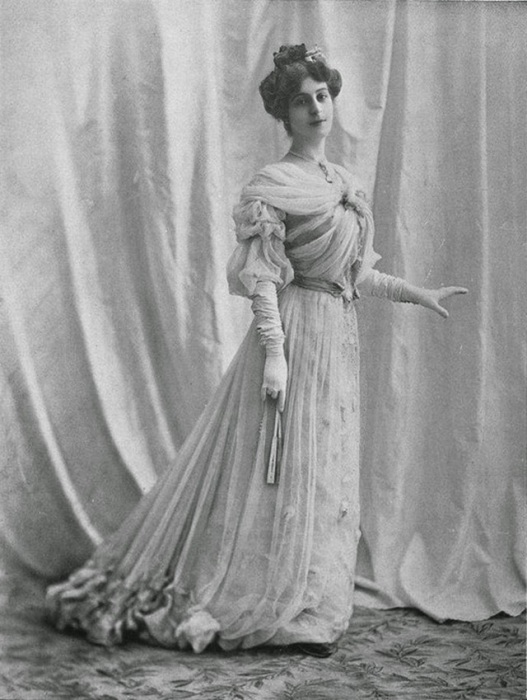 Девушка в платье украшенным драпировками на лифе и юбке.