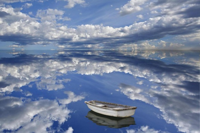 Лодка на прозрачной воде, в которой отражается небо.