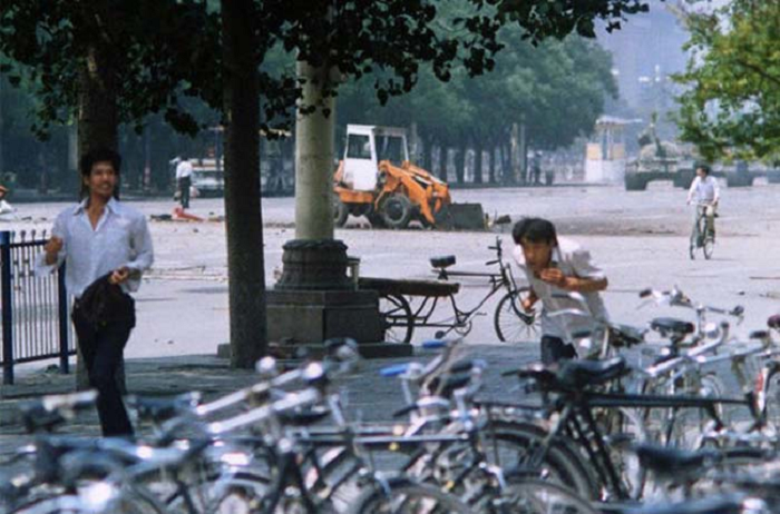 Трое неизвестных спасаются бегством, в то время как человек на заднем плане пытается загородить дорогу приближающимся танкам. 4 июня 1989 года.