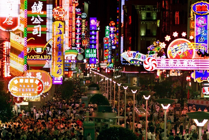 Покупатели толпятся под красочными неоновыми огнями вдоль оживленной Нанкинской улицы Шанхая.