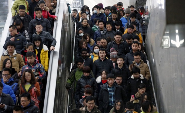 Люди спускаются на эскалаторе и сходят по лестнице, направляясь к платформе метро в час пик в Пекине.